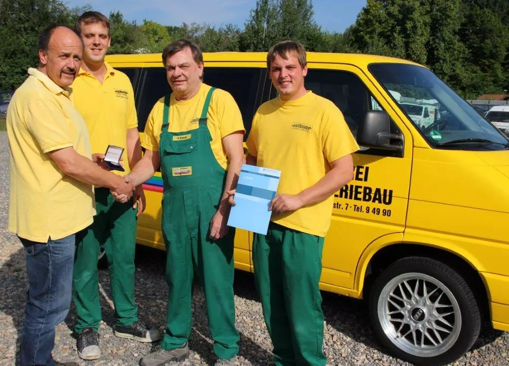 Drei Männer in gelben Overalls stehen neben einem Lieferwagen.